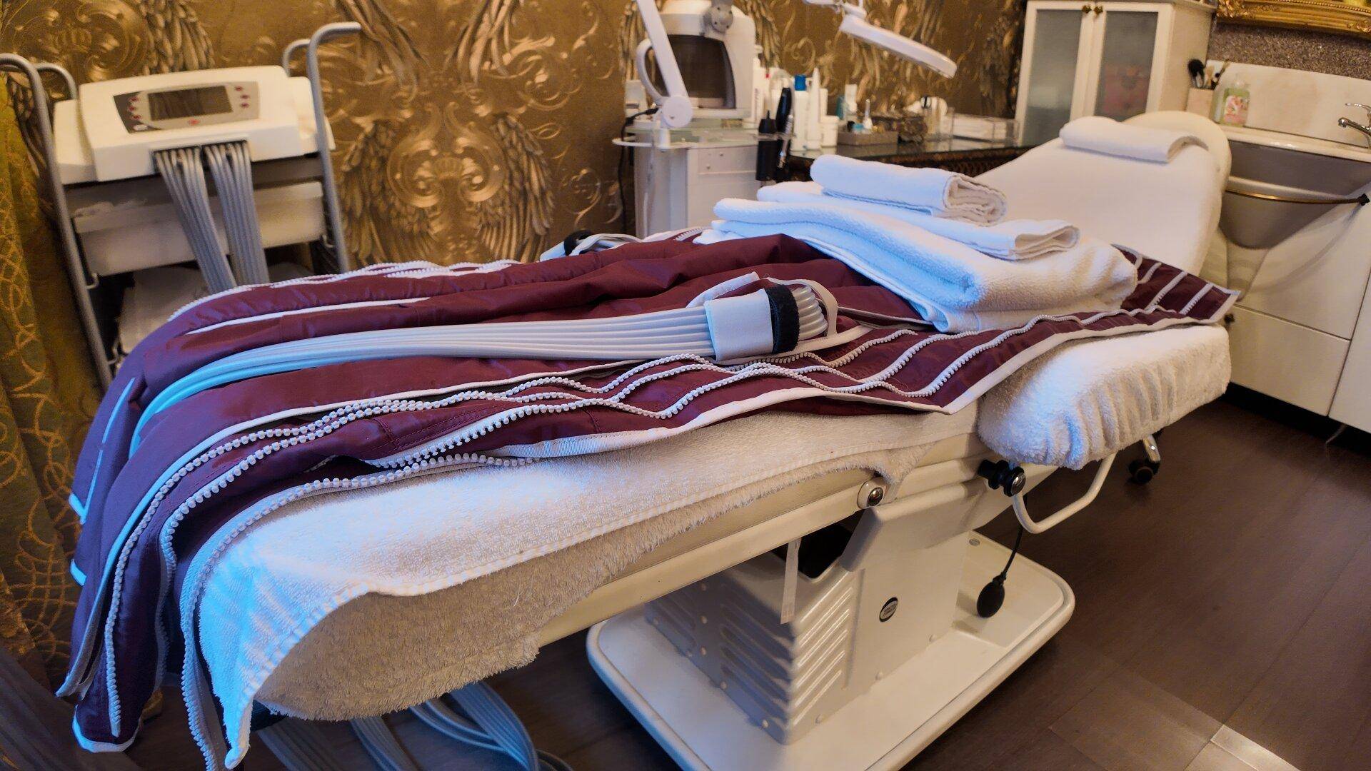 Nahaufnahme einer Massageliege mit einer roten Decke und einem Behandlungsgerät.