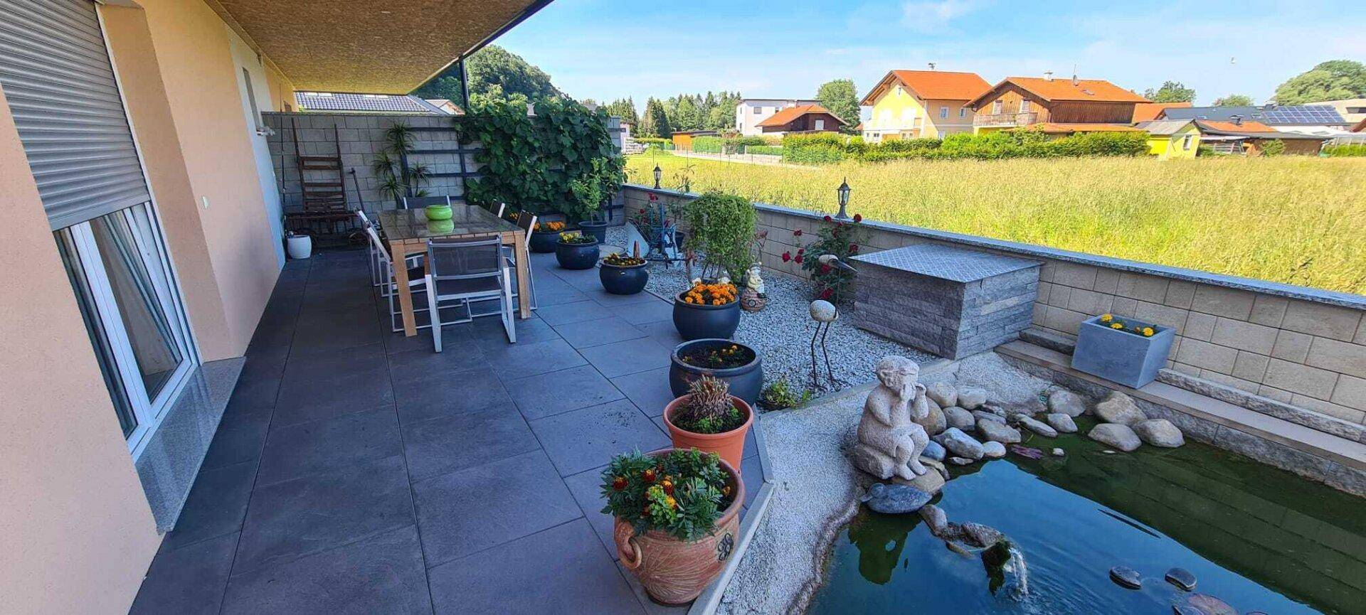 Geräumige Terrasse mit Esstisch, Teich und dekorativen Elementen im Gartenbereich.