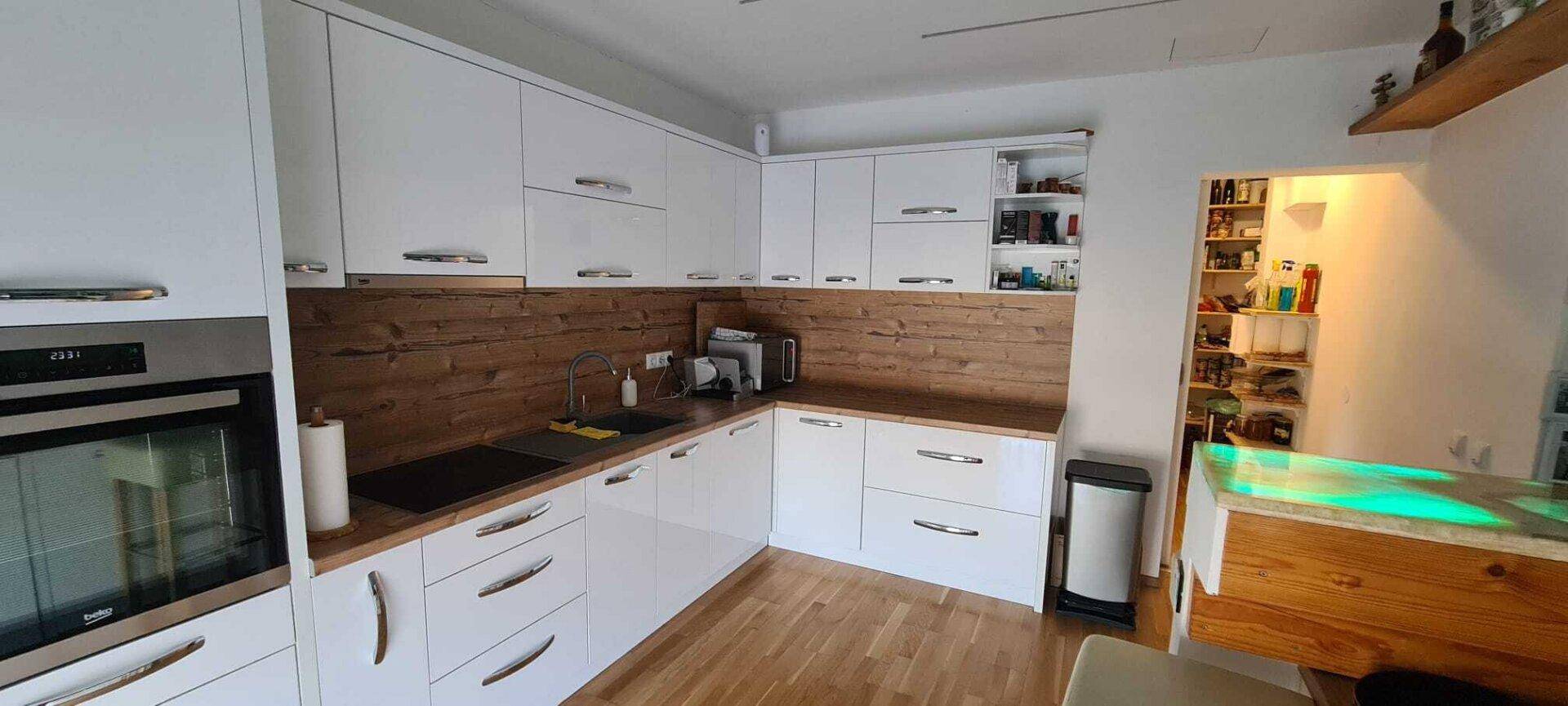 Moderne Küche mit weißen Hochglanzfronten, Holzakzenten und integrierten Geräten.