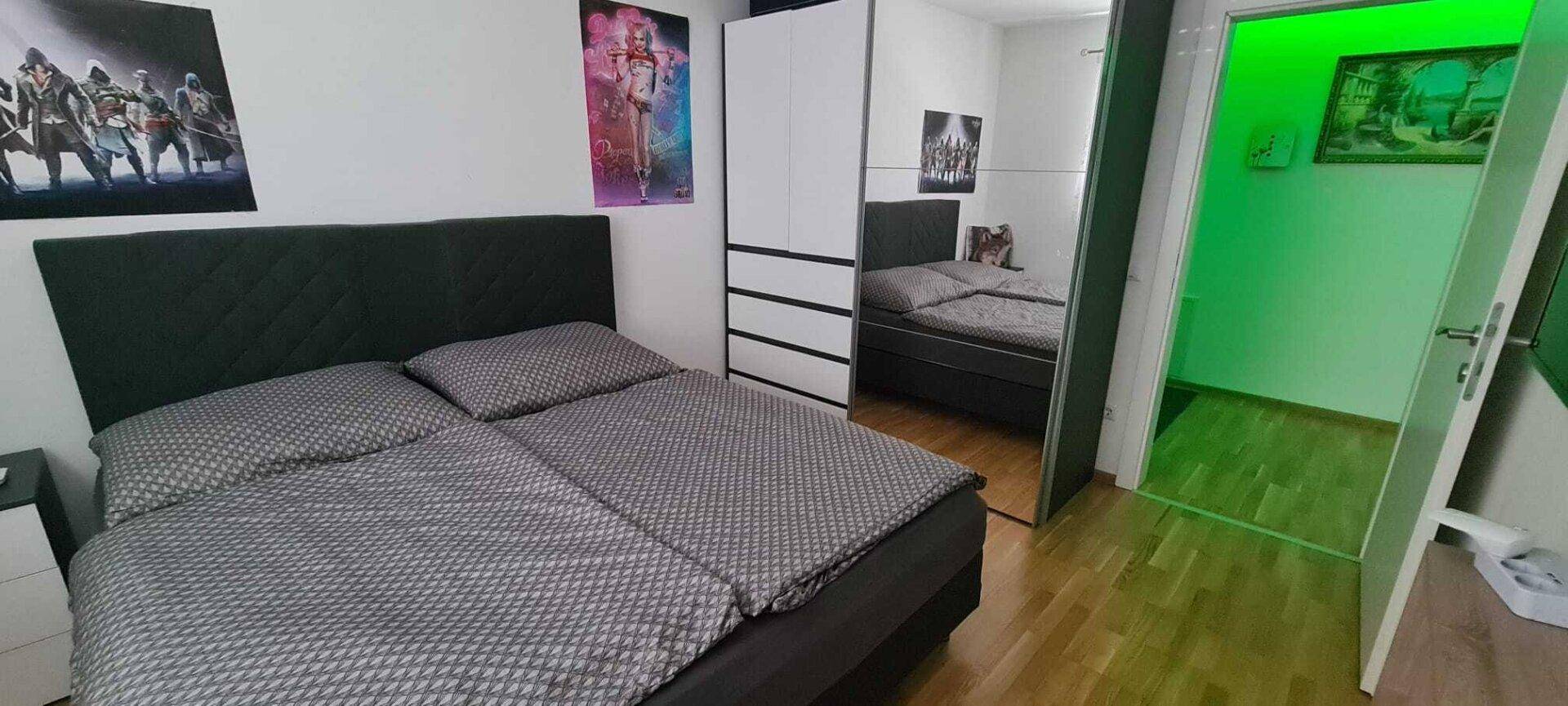 Helles Schlafzimmer mit Doppelbett, Kleiderschrank und Zugang zu einem weiteren Raum.
