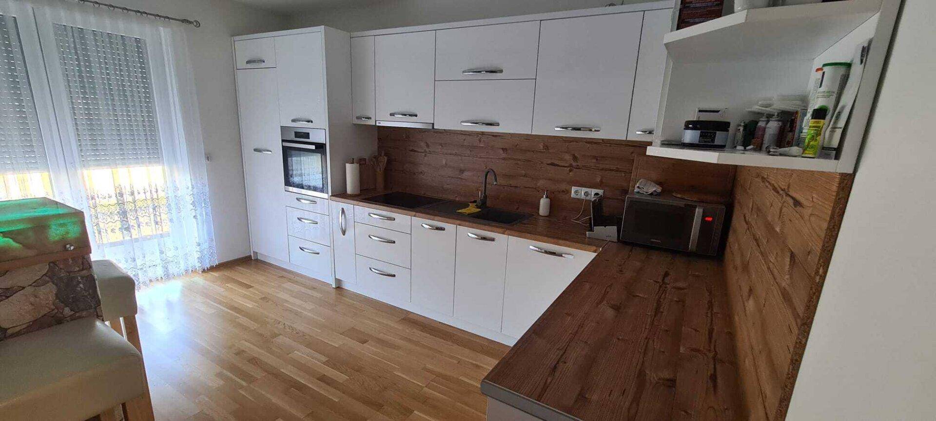 Moderne Küche mit weißen Schränken, Holzarbeitsplatten und Fenster mit Jalousien.