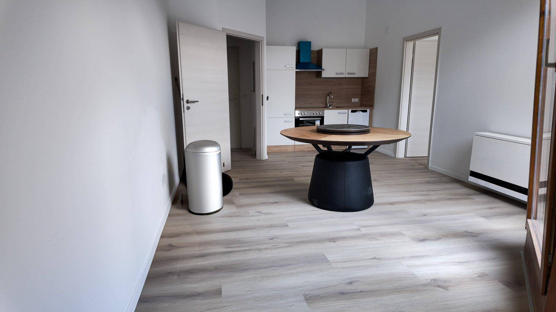 Offener Raum mit kleiner Küchenzeile, Laminatboden und einem runden Holztisch.