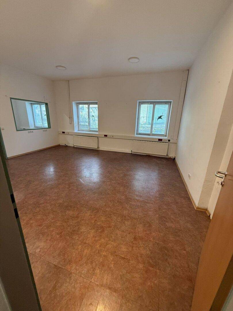 Leerer Raum mit braunem Linoleumboden, weißen Wänden und zwei Fenstern, ideal als Büro.