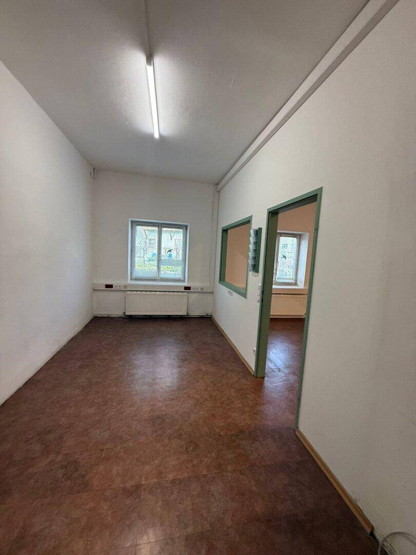 Geräumiger, leerer Raum mit Linoleumboden, weißen Wänden und Zugang zu einem weiteren Zimmer.