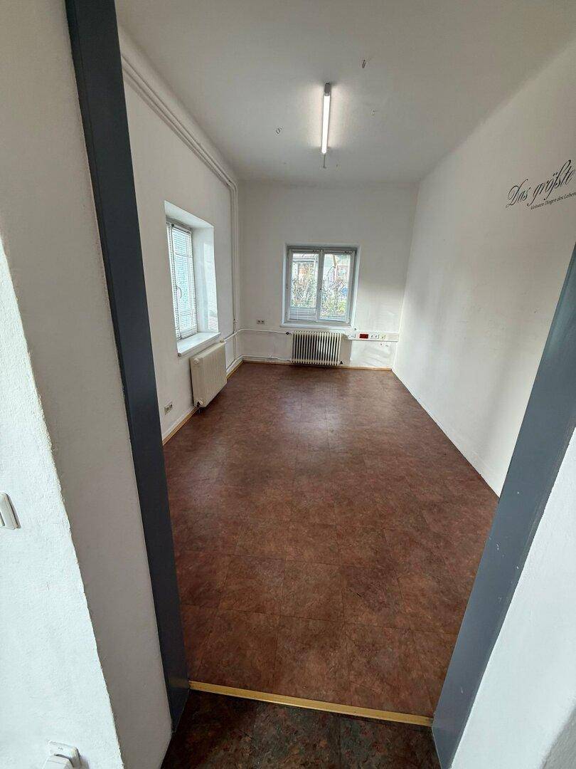Heller, leerer Raum mit Linoleumboden und zwei Fenstern, geeignet für verschiedene Nutzungen.
