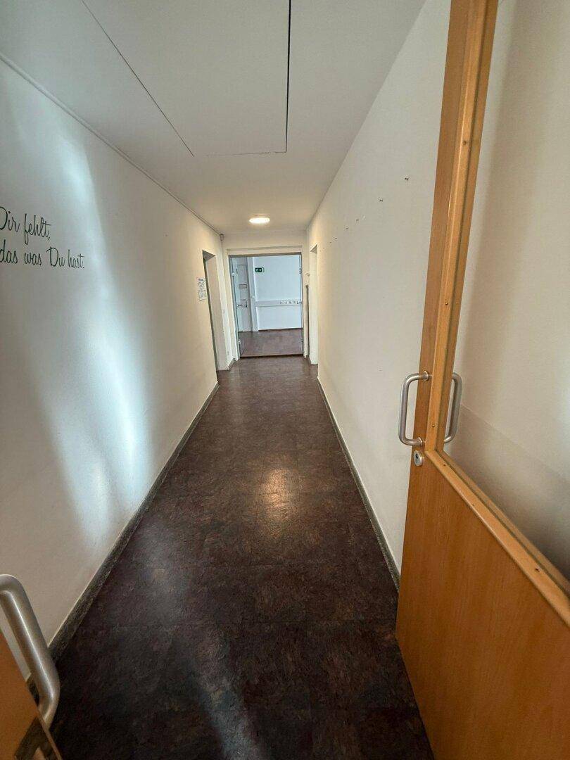 Langer Flur mit Holztüren und Linoleumboden, der zu weiteren Räumen führt.