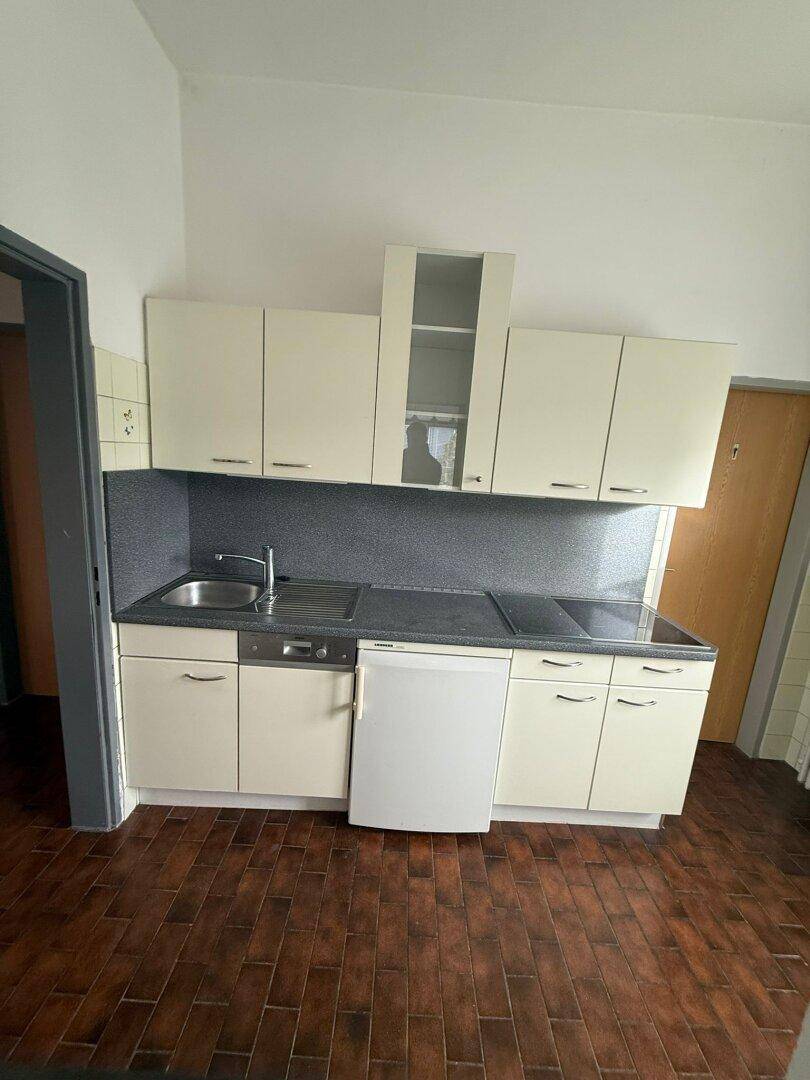 Kleine Küchenzeile mit hellen Schränken, dunkler Arbeitsplatte, Spüle und integrierten Geräten.