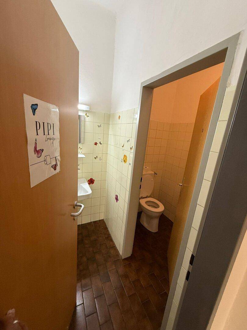 Kleine Toilette mit Waschbecken, WC und hell gefliesten Wänden sowie dunklem Fliesenboden.