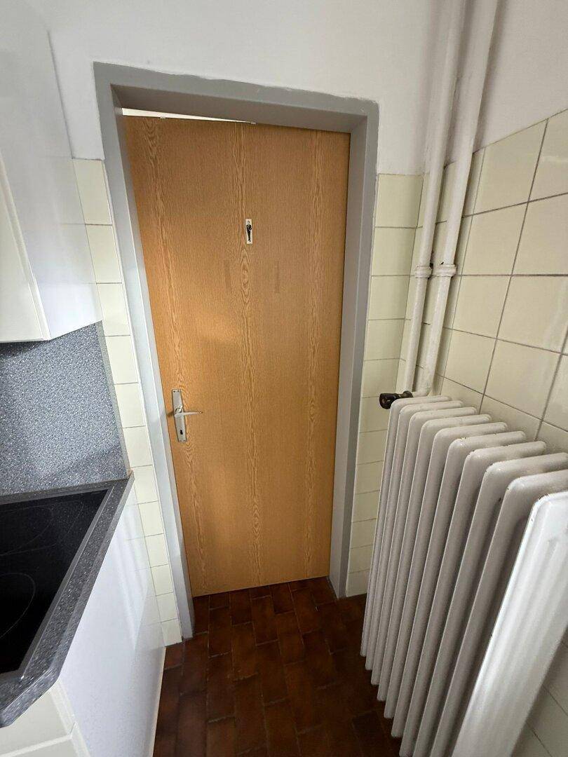 Holztür in einem gefliesten Bereich mit Heizkörper, möglicherweise zu einem Abstellraum führend.