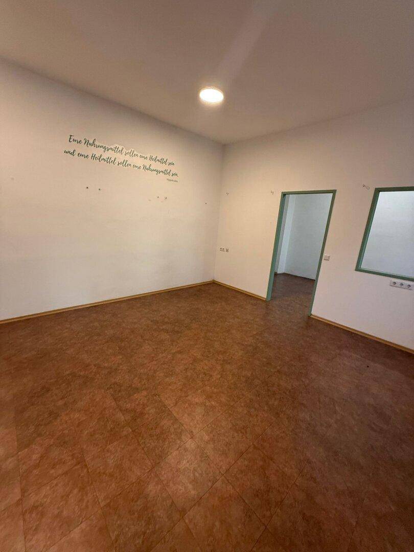 Geräumiger, leerer Raum mit Linoleumboden und weißen Wänden, offen zu einem weiteren Bereich.