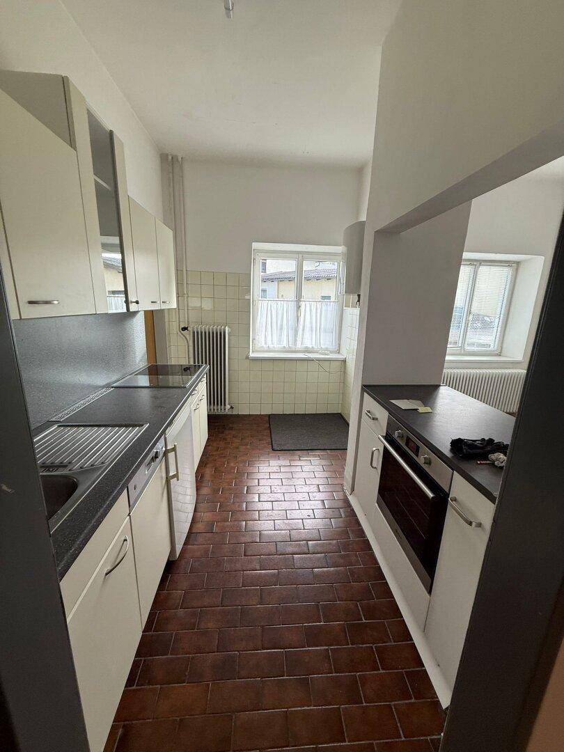 Schmale Küche mit weißen Schränken, dunklen Arbeitsplatten, gefliesten Wänden und einem Fenster.