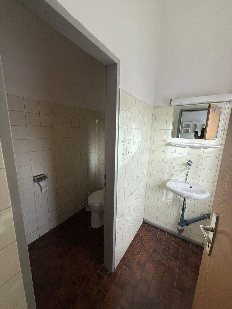 Kleine Toilette mit Waschbecken, WC und hell gefliesten Wänden sowie dunklem Fliesenboden.