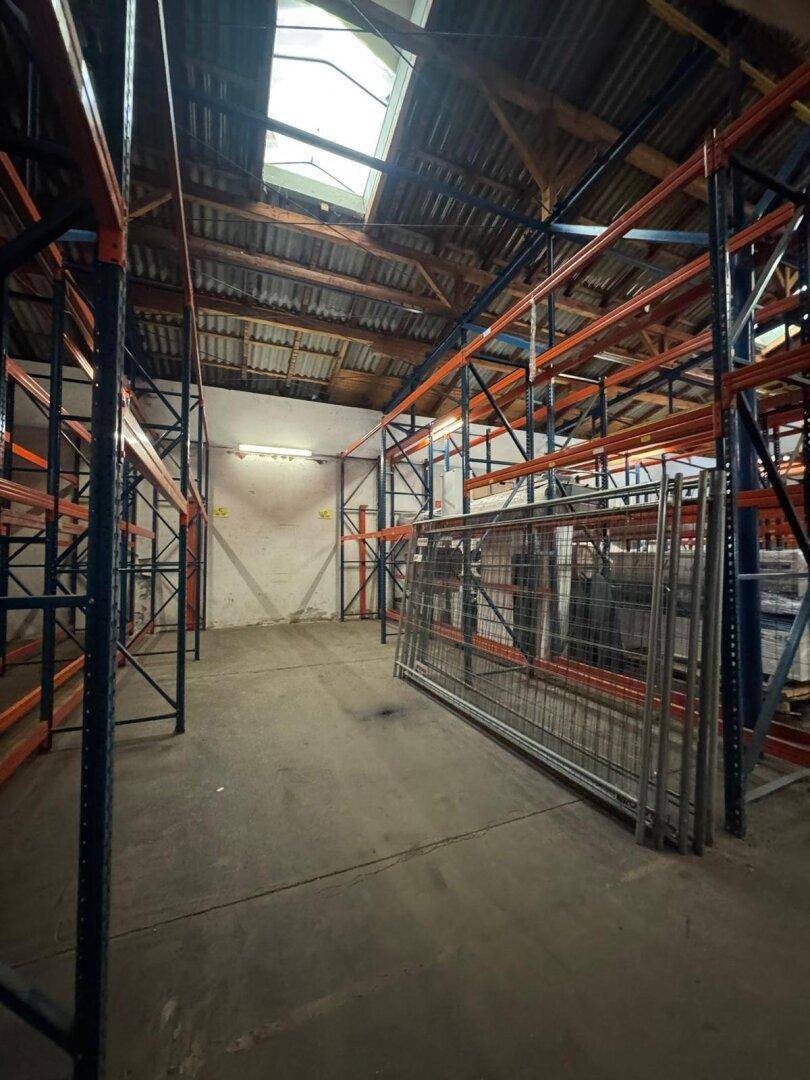 Lagerhalle mit hohen Regalen, Betonboden und sichtbarer Dachkonstruktion, mit Oberlichtern für Tageslicht. Die Halle ist leer.