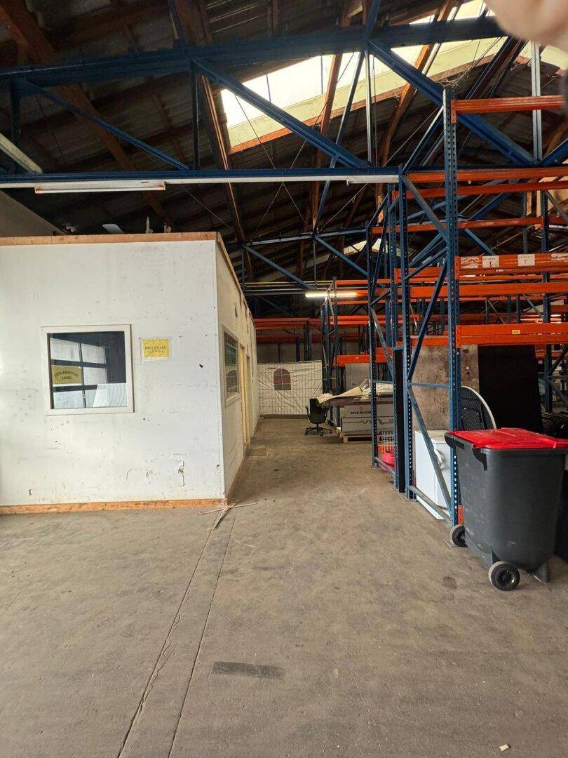Geräumige Lagerhalle mit hohen Decken, Betonboden und robusten Metallregalen, inklusive eines kleinen Bürobereichs.