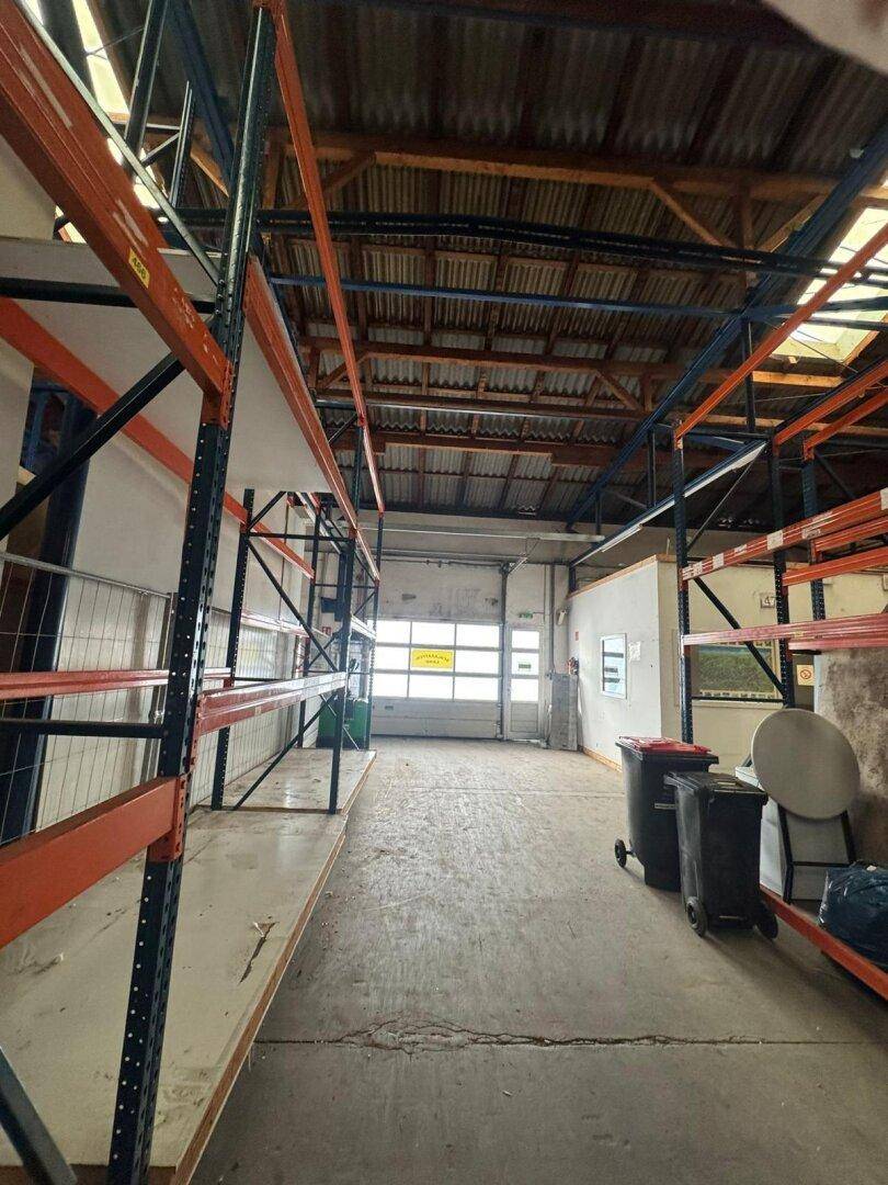 Weitläufige Lagerhalle mit hohen Decken, Betonboden und Zugang über ein großes Rolltor am Ende des Raumes.