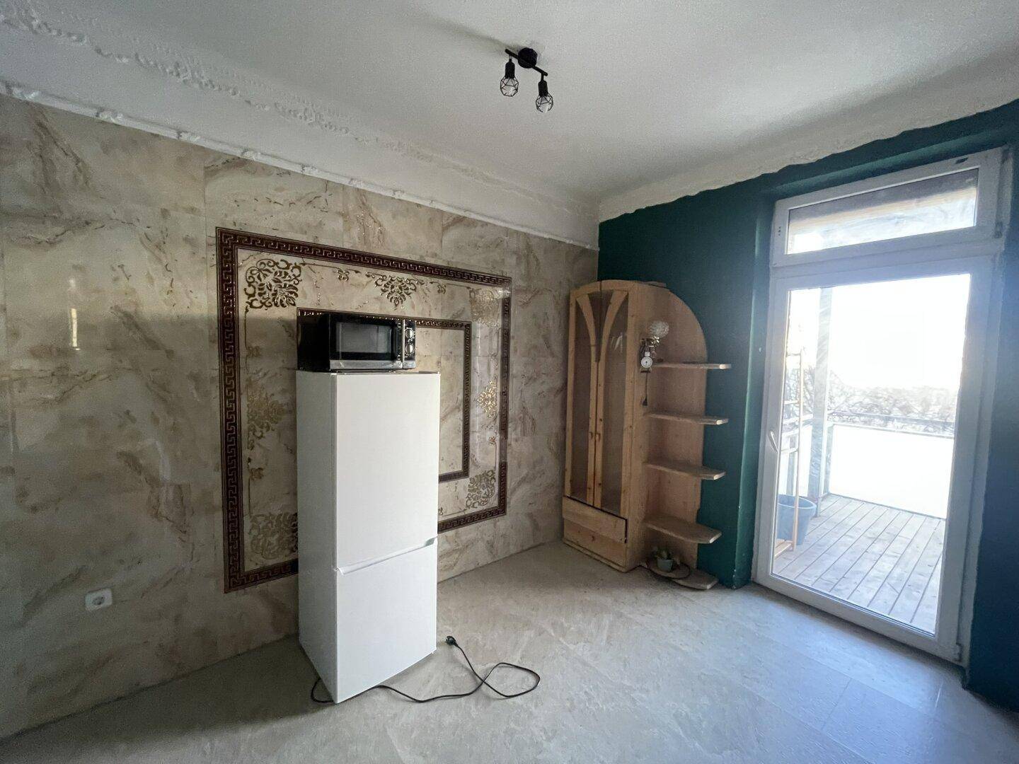 Zimmer mit Zugang zum Balkon, Kühlschrank und Mikrowelle, teilweise gefliesten Wänden.