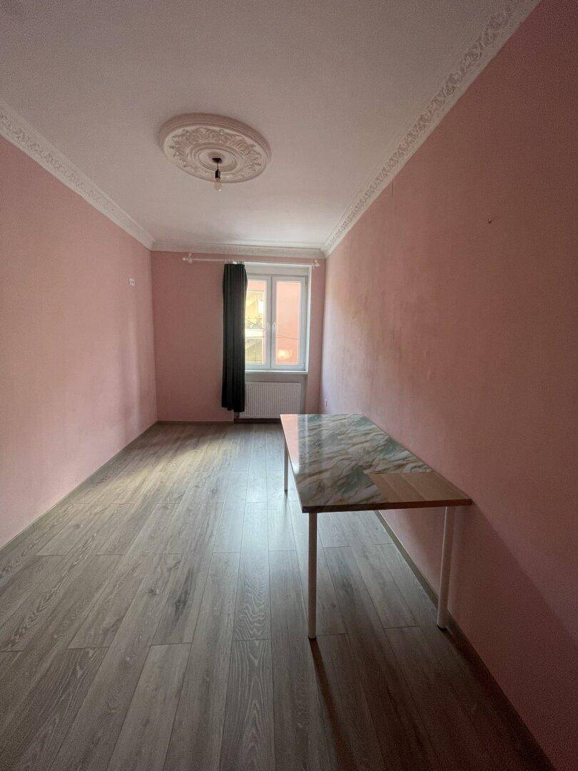 Leeres Zimmer mit rosa Wänden, Laminatboden und dekorativer Deckenrosette.