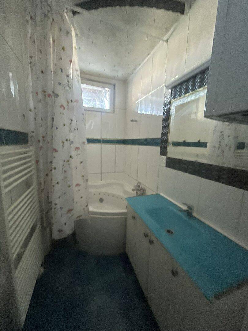 Kleines Badezimmer mit Eckbadewanne, Waschbecken und Fliesen an Wänden und Boden.