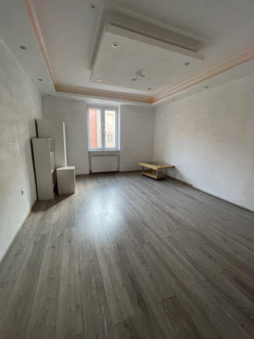 Helles, leeres Zimmer mit modernem Laminatboden und Stuckdecke.