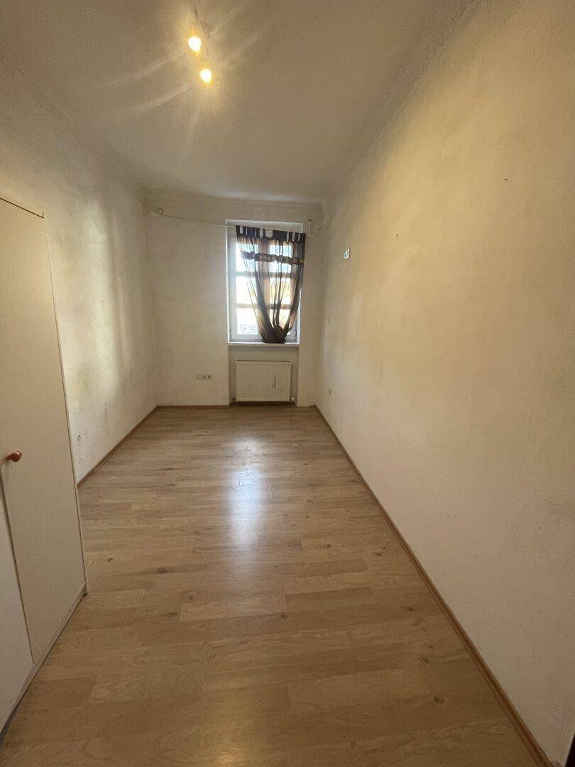 Helles, leeres Zimmer mit hellem Laminatboden und Fenster.