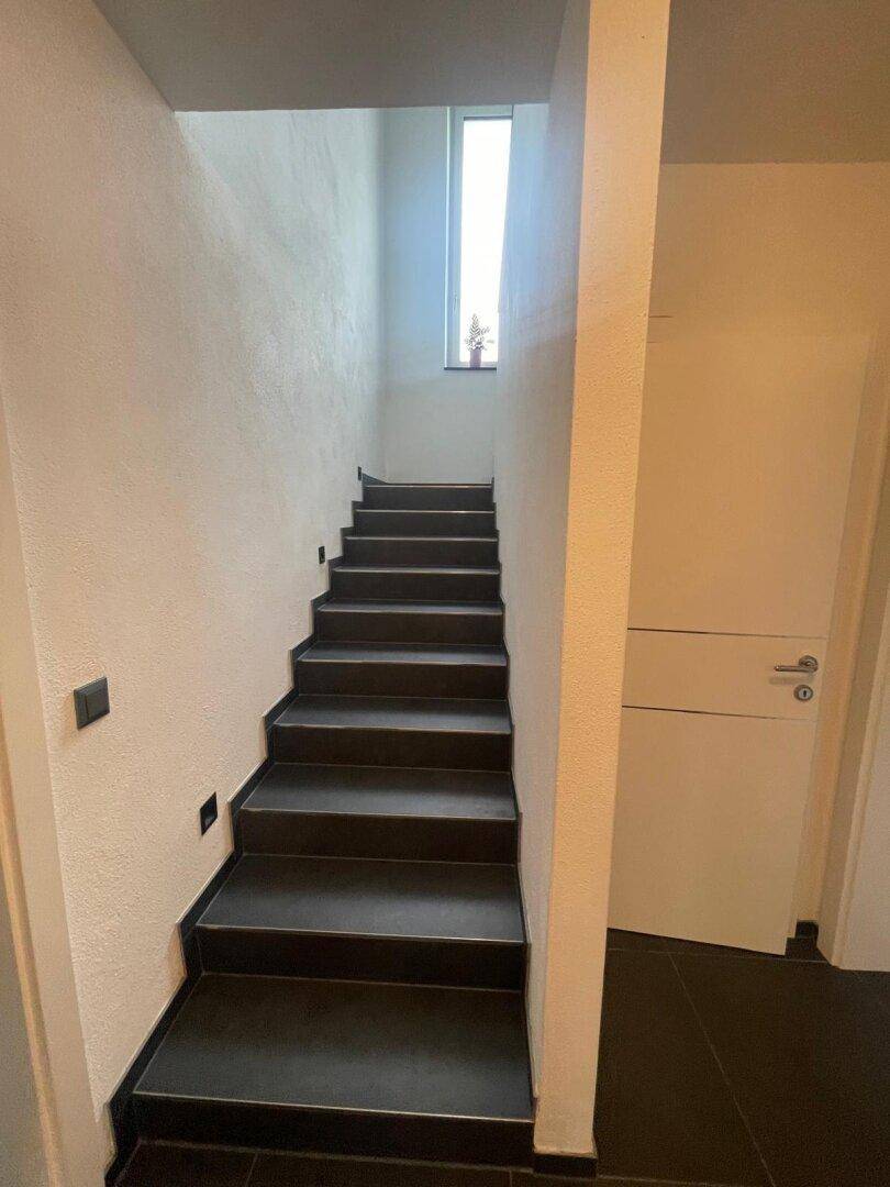 Moderne Treppe mit dunklen Stufen und hellem Fenster für natürliches Licht im Treppenhaus.