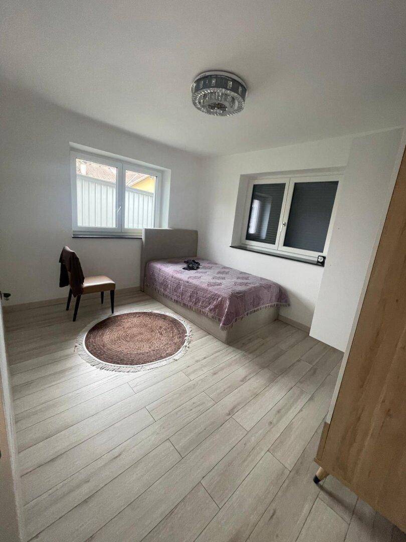 Helles Schlafzimmer mit Einzelbett, Holzoptikboden und zwei Fenstern für gute Belüftung.