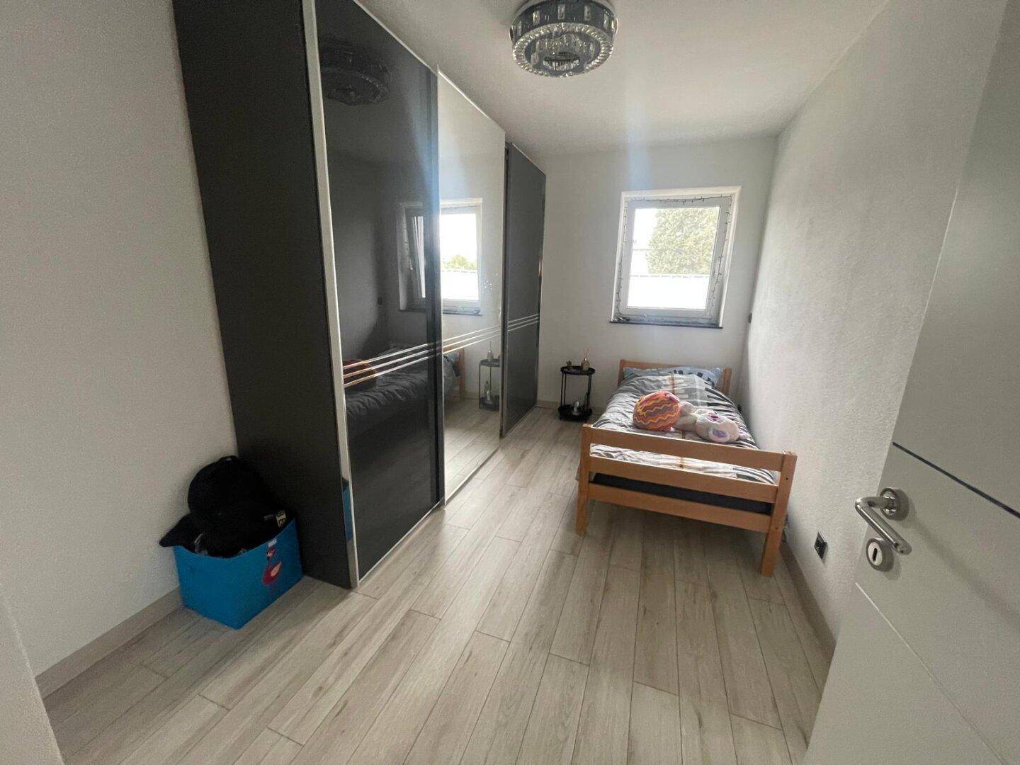 Kleines Schlafzimmer mit Einzelbett, Spiegelschrank und Holzoptikboden, ideal für Kinder.