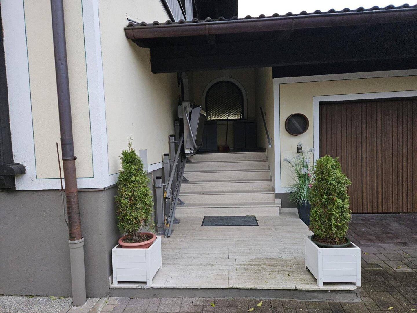 Hauseingang mit Treppe, Topfpflanzen und einer Holztür zur Garage.