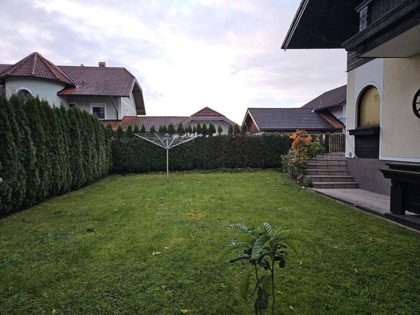 Weiter Rasenbereich mit Wäschespinne und umgebenden Hecken unter bewölktem Himmel.