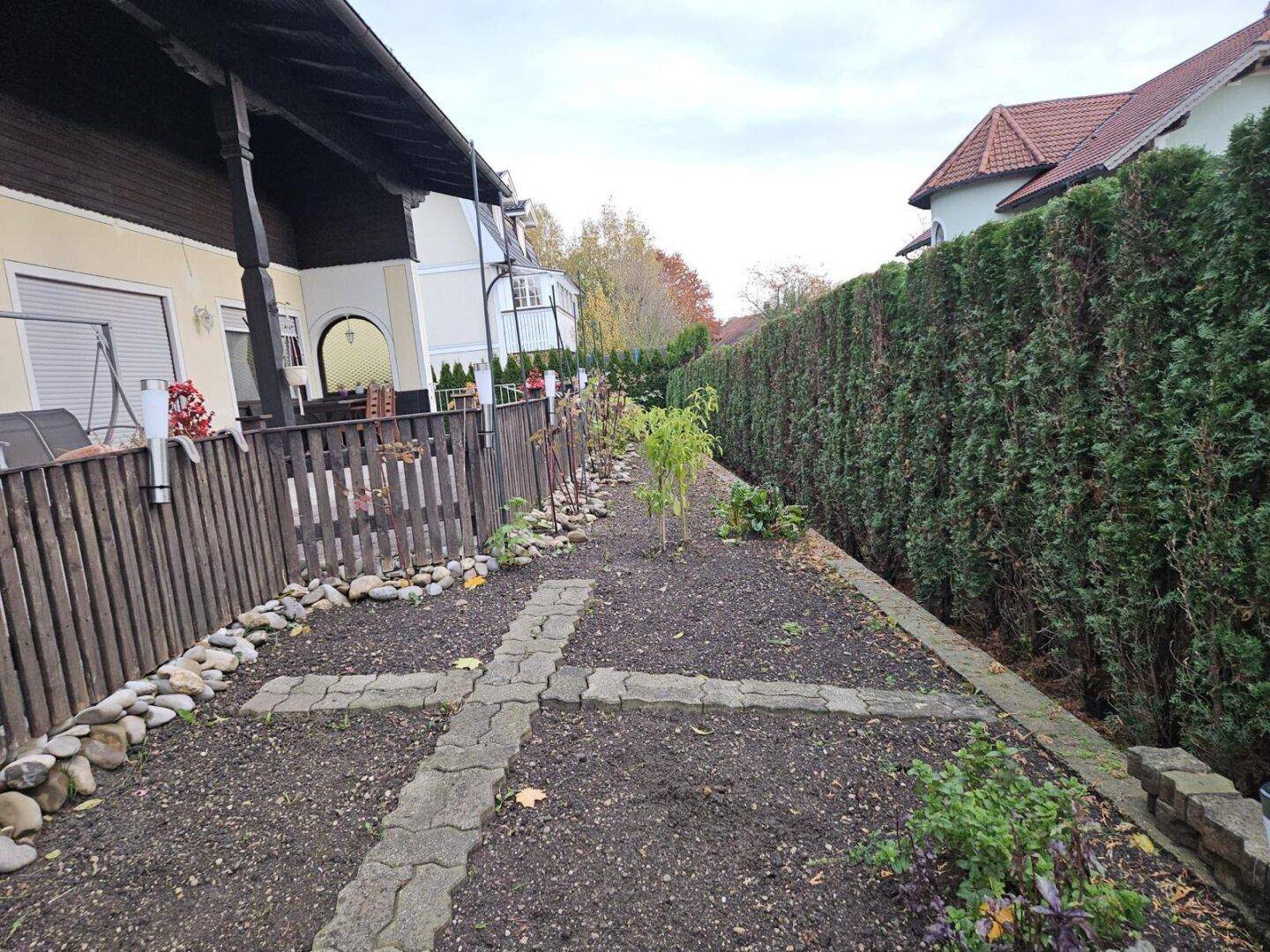 Gartenweg mit bepflanzten Beeten und einer hohen Hecke als Abgrenzung.