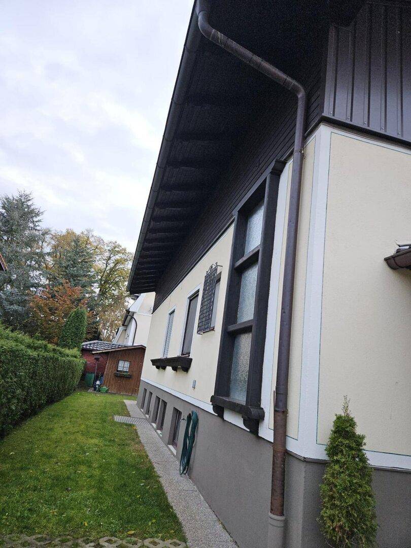 Seitenansicht des Hauses mit Fenstern, Fallrohr und gepflegtem Rasen.
