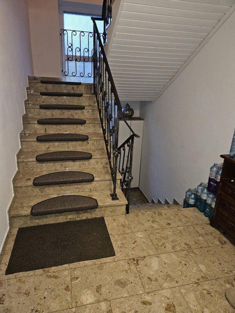 Marmortreppe mit schmiedeeisernem Geländer und Fliesenboden im Eingangsbereich.