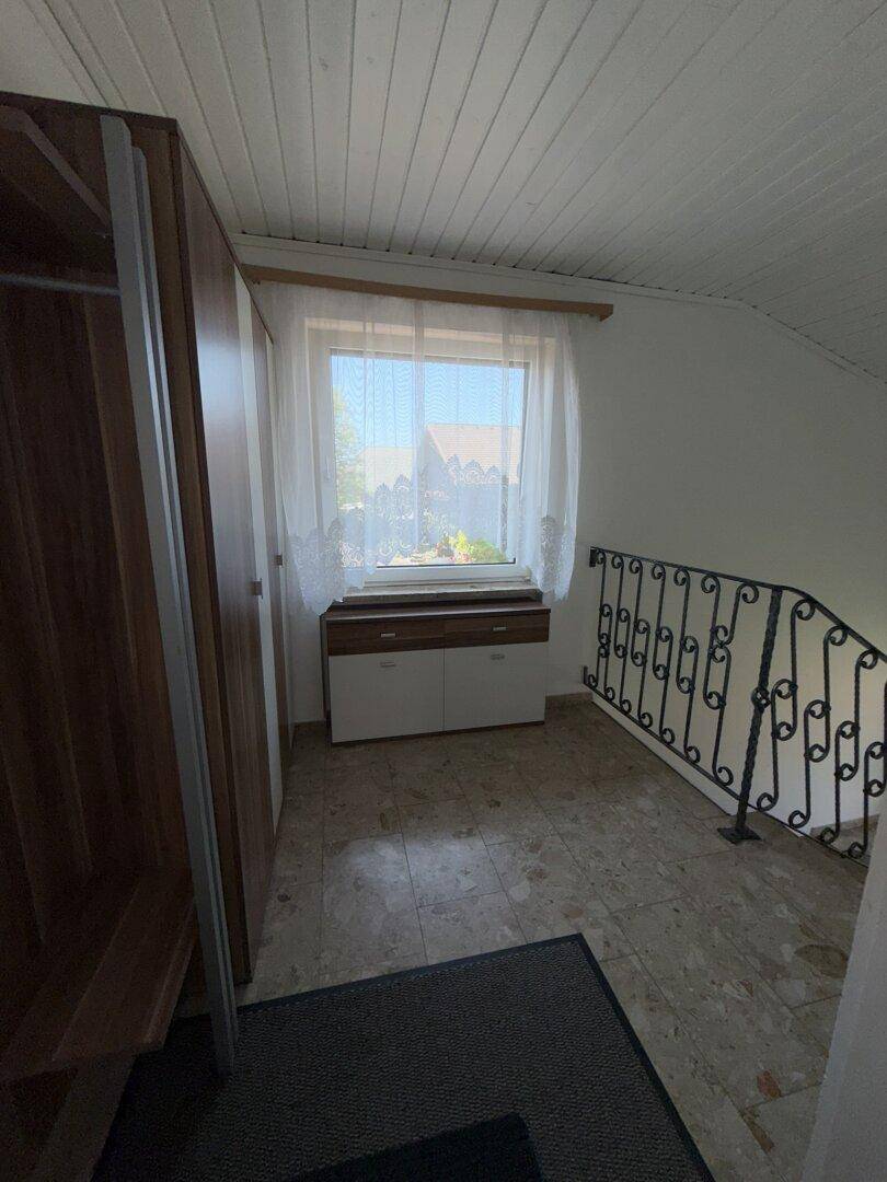 Dachgeschossbereich mit Fenster, Schrank und schmiedeeisernem Treppengeländer, das in ein anderes Stockwerk führt.