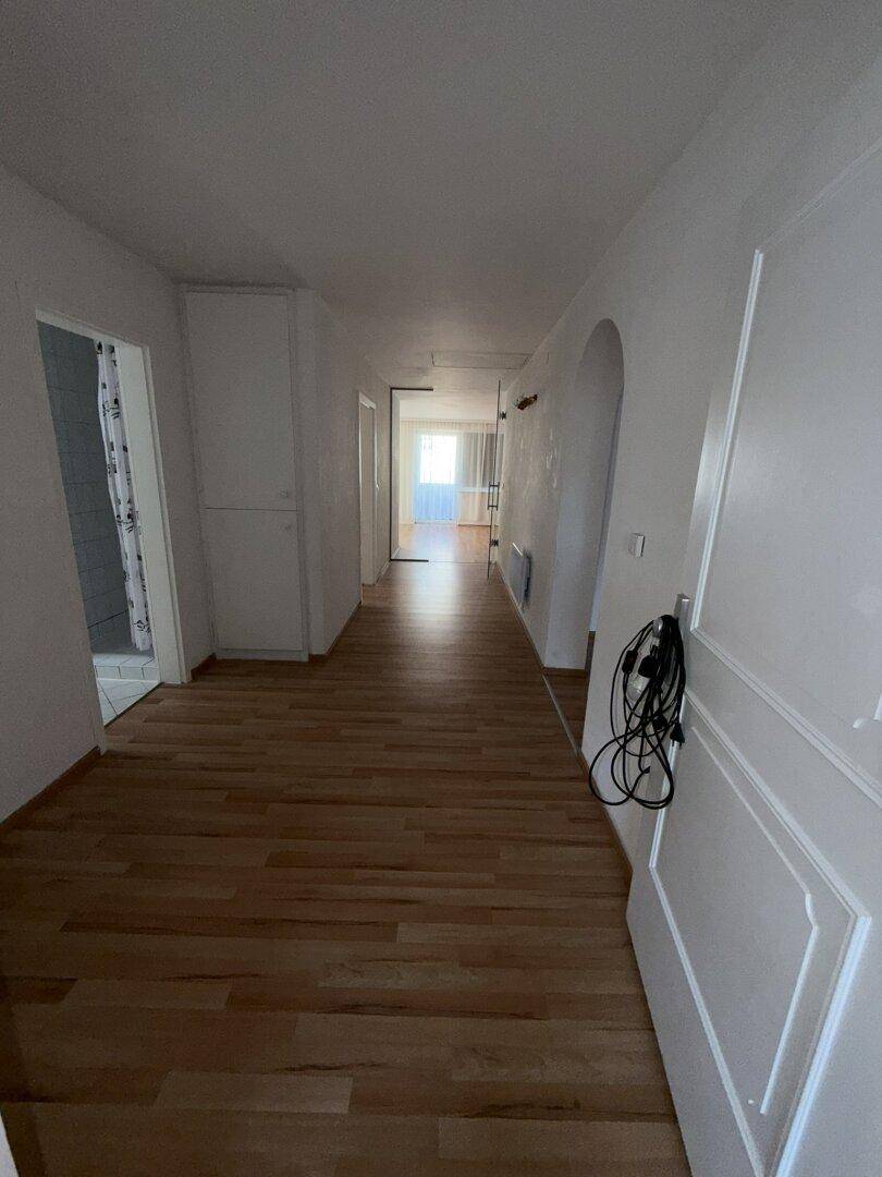 Langer, heller Flur mit Laminatboden, der zu verschiedenen Räumen und einem Badezimmer führt.