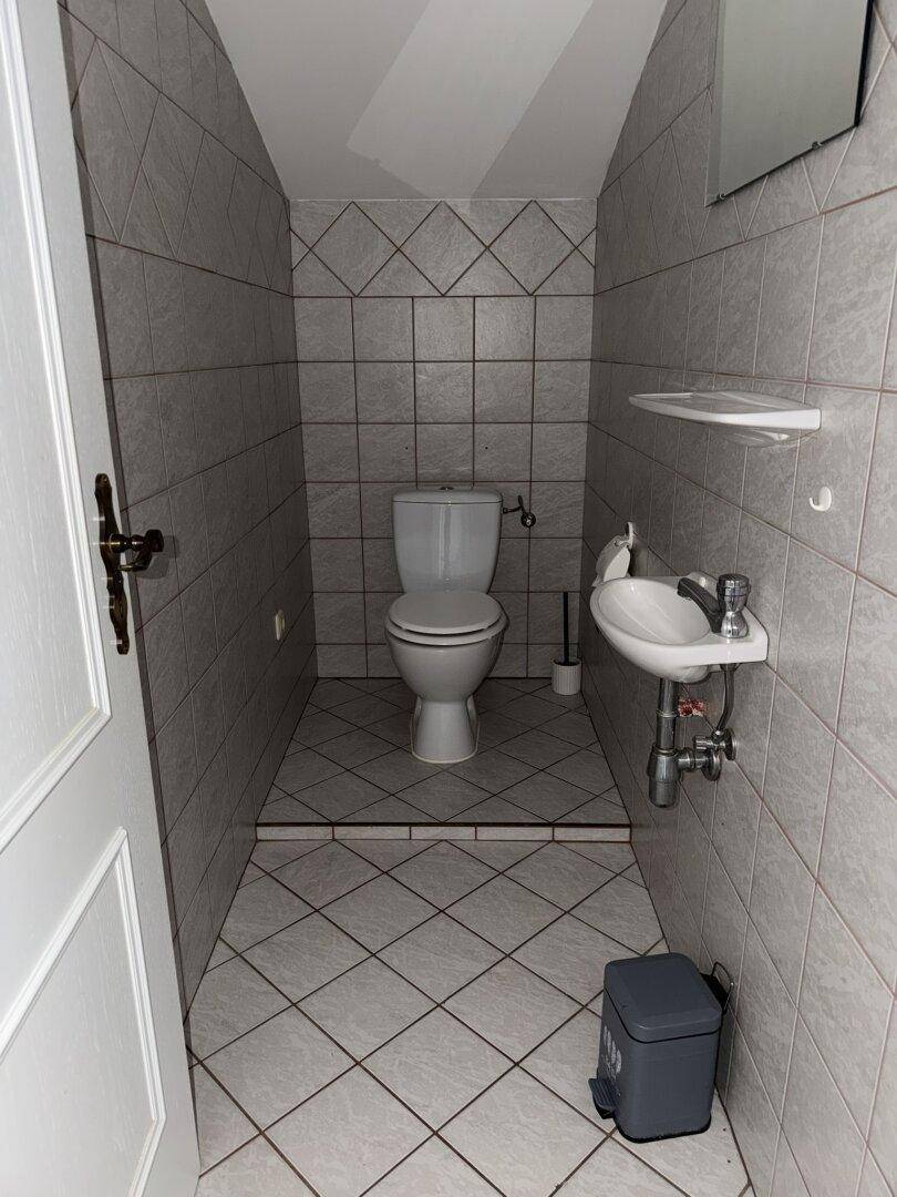 Kleines Gäste-WC mit hellgrauen Fliesen an Wänden und Boden sowie einem einfachen Waschbecken.