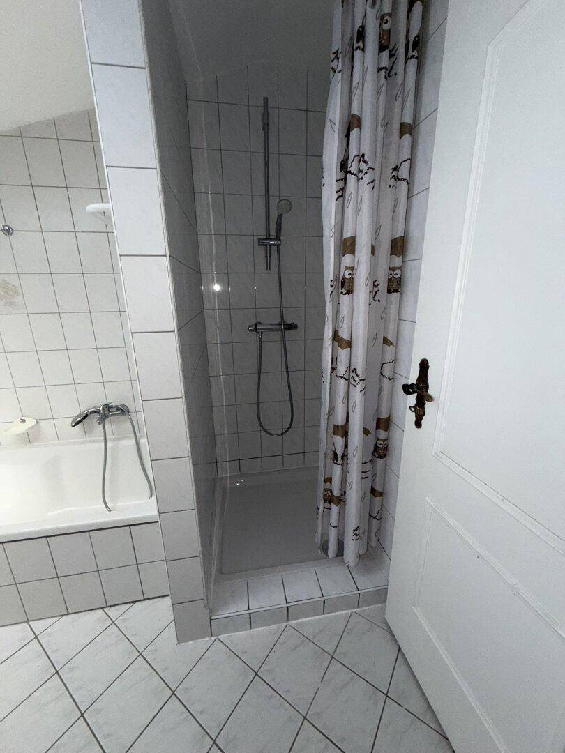 Badezimmer mit Badewanne und separater Duschkabine, ausgestattet mit weißen Fliesen und Duschvorhang.