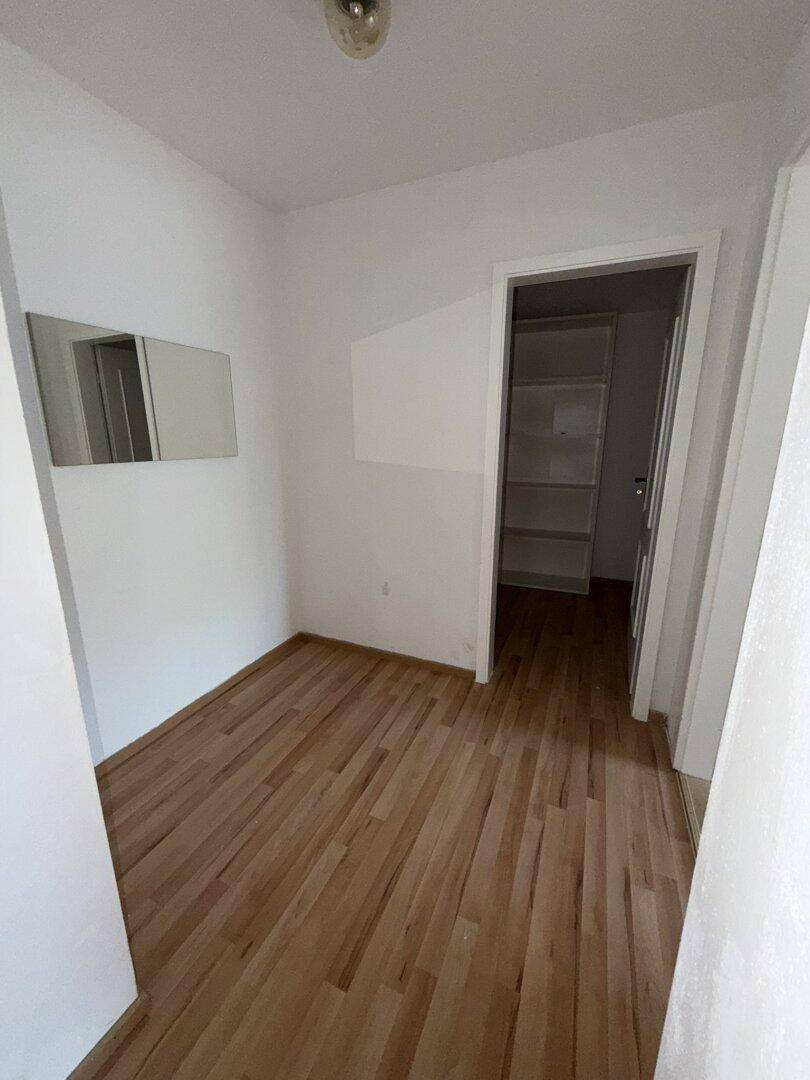 Kleines Zimmer mit Laminatboden und einem Spiegel an der Wand, ideal als Schlaf- oder Arbeitszimmer.