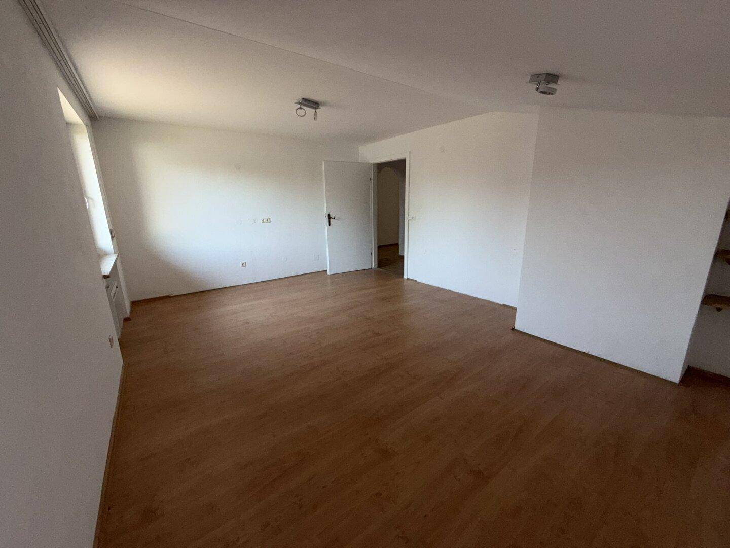 Geräumiges Wohnzimmer mit Laminatboden und weißen Wänden, bereit zur individuellen Gestaltung.