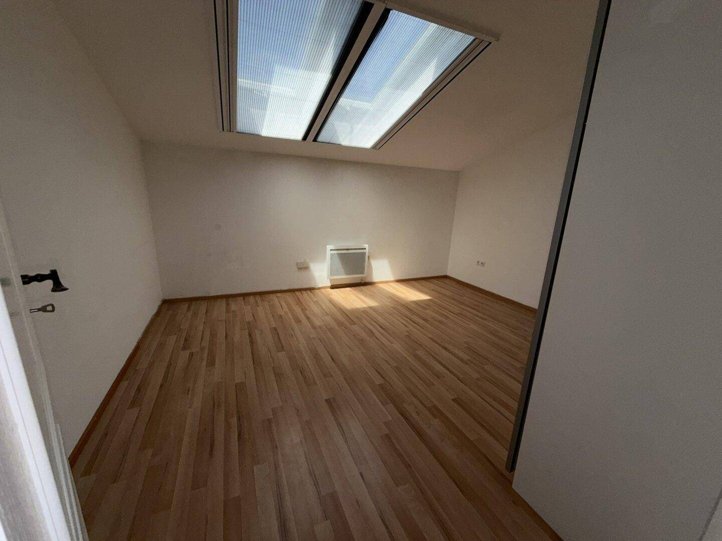 Helles Schlafzimmer mit Laminatboden und großem Dachfenster, das viel Licht spendet.