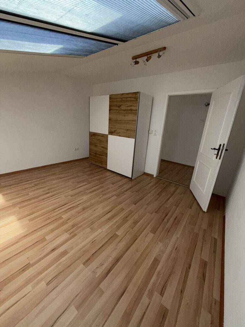 Schlafzimmer mit Laminatboden, Dachfenster und einem modernen Kleiderschrank mit Holz- und Weißtönen.