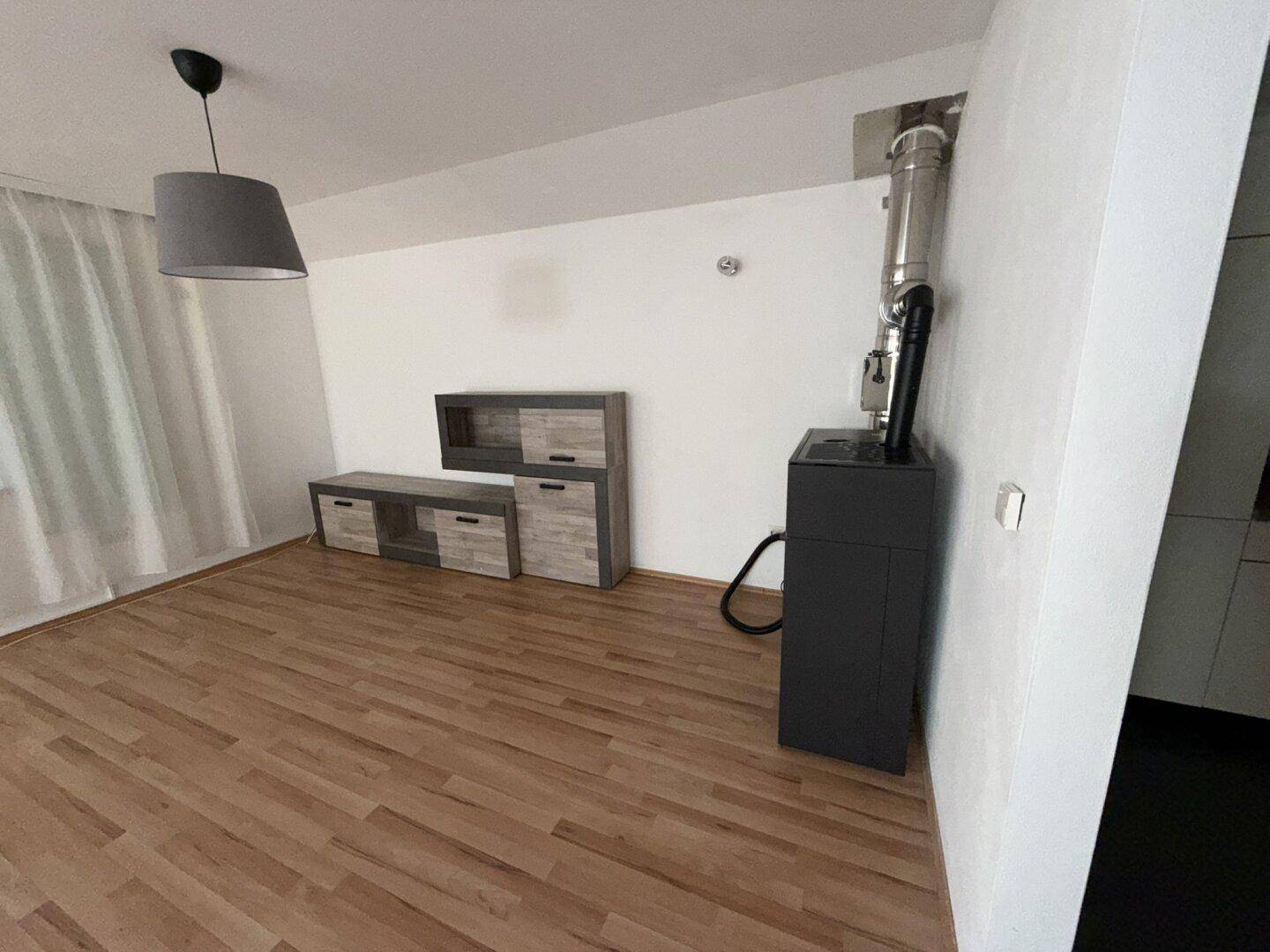 Heller Wohnbereich mit Laminatboden, modernem Holzofen und einer Pendelleuchte.