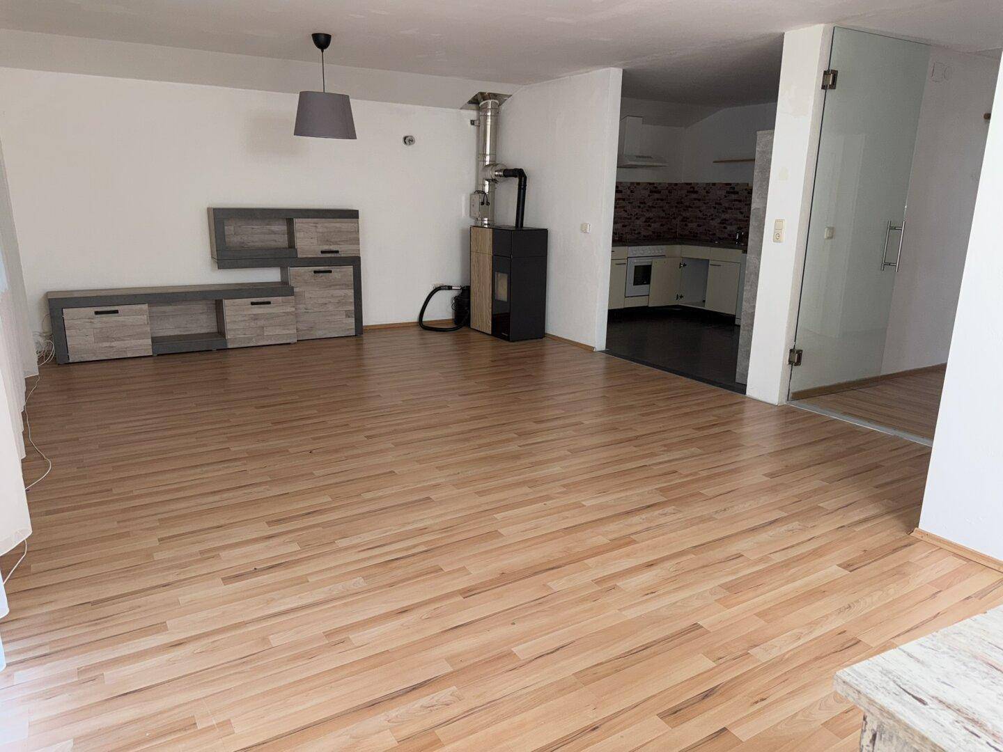 Offener Wohnbereich mit Laminatboden, Holzofen und Blick auf die angrenzende Küche.