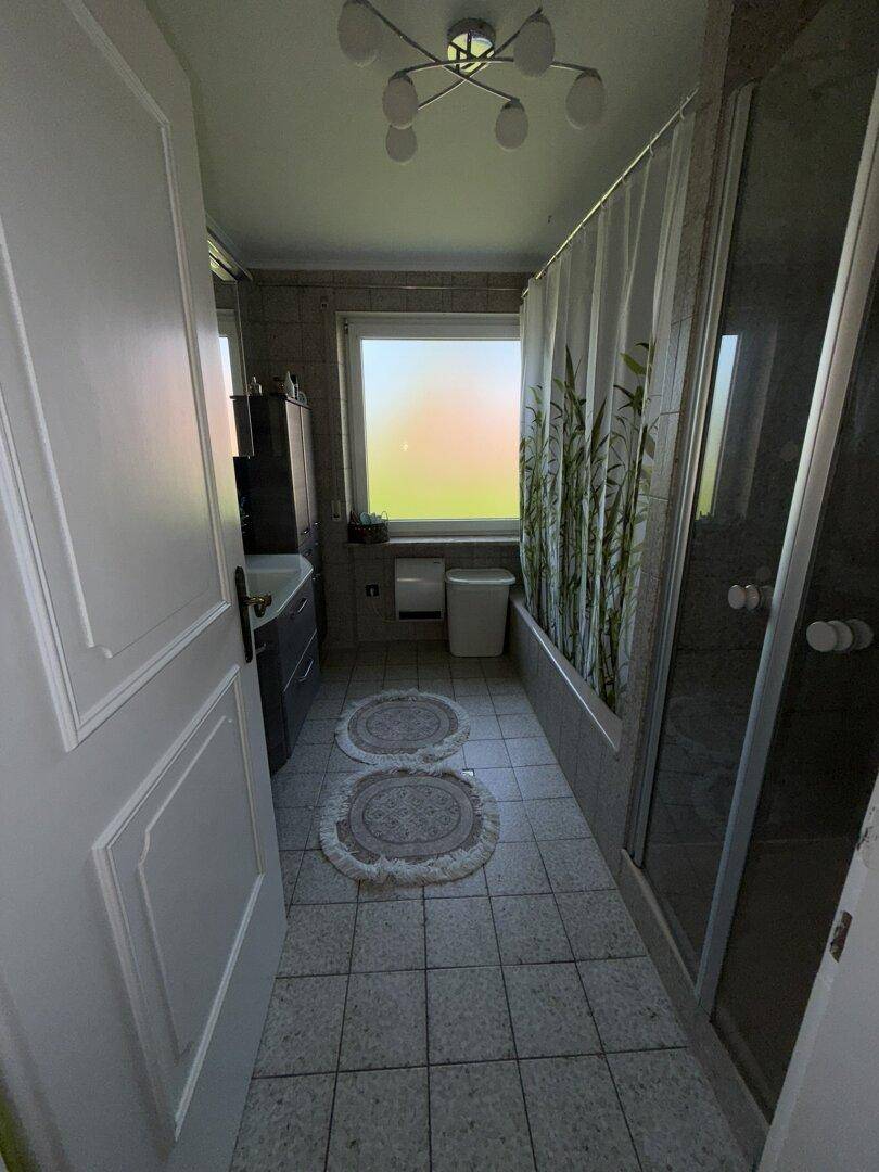 Badezimmer mit Badewanne, Duschkabine und Fenster, ausgestattet mit hellen Fliesen.