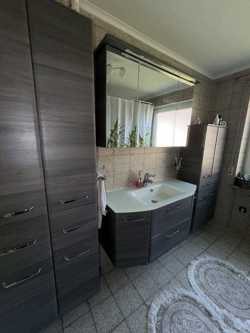 Badezimmer mit modernem Waschtisch, Spiegelschrank und hohen Schränken in dunklem Holzdekor.