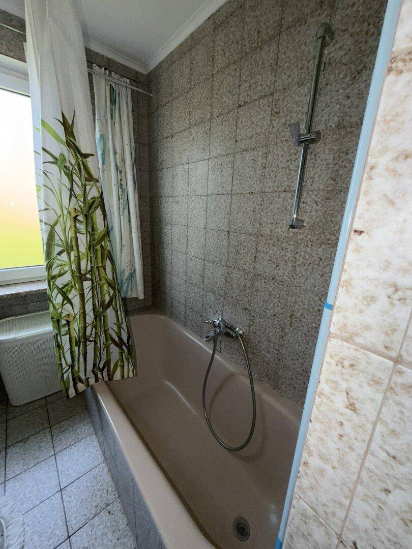 Badezimmer mit Badewanne und Duschvorhang, hellen Fliesen und einem Fenster.