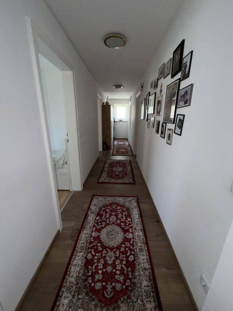 Langer, heller Flur mit Laminatboden, traditionellen Teppichen und gerahmten Bildern an der Wand.