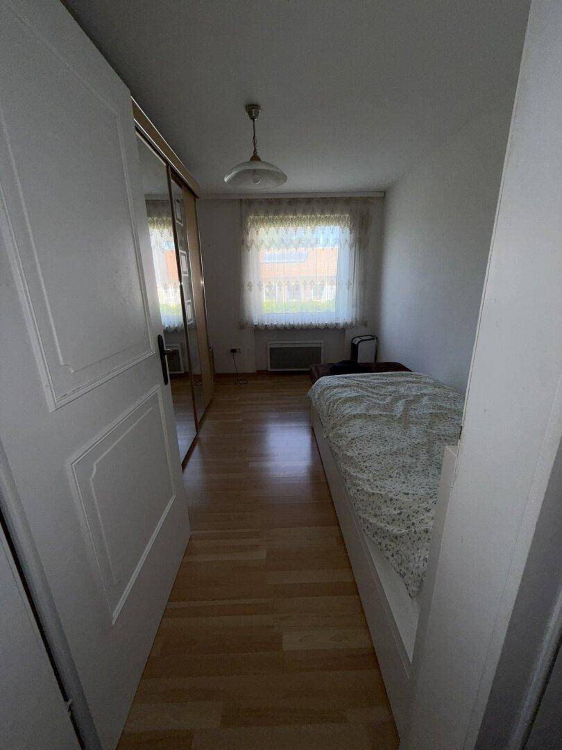 Schlafzimmer mit Einzelbett, Laminatboden und großem Spiegelschrank, der den Raum optisch vergrößert.
