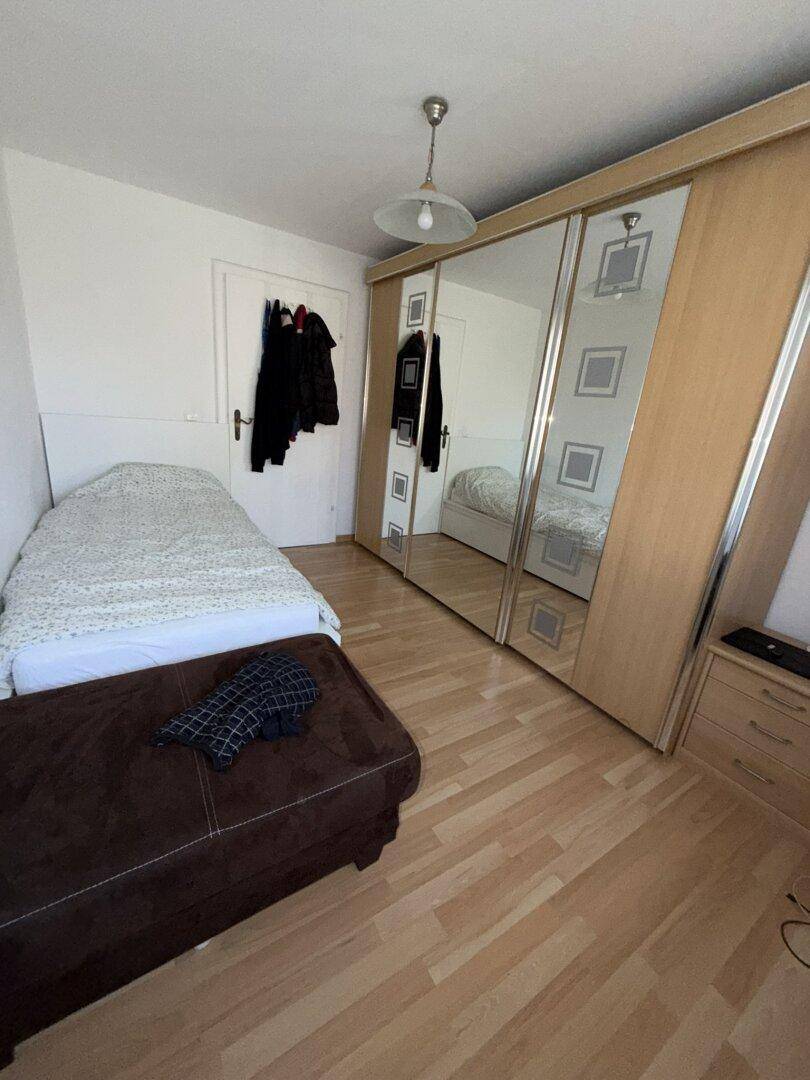 Schlafzimmer mit Einzelbett, Laminatboden und großem Spiegelschrank, der viel Stauraum bietet.