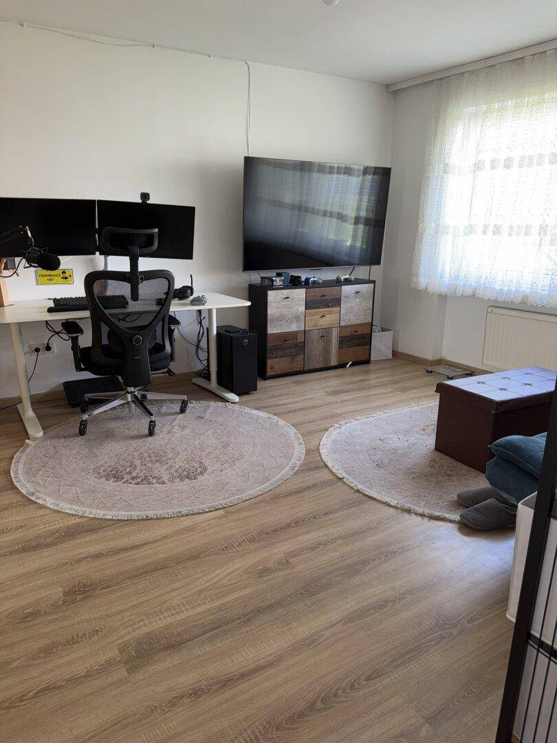 Geräumiges Zimmer mit Laminatboden, großem Schreibtisch und Fernseher, ideal als Büro oder Wohnzimmer.