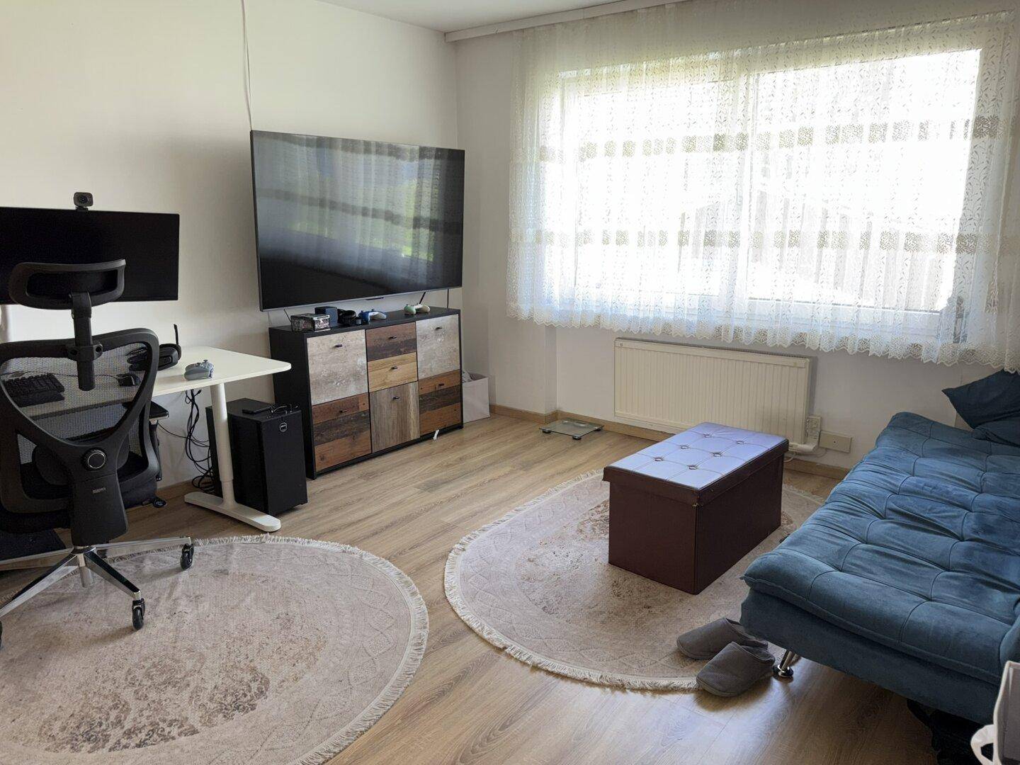 Heller Wohnbereich mit Laminatboden, Sofa und großem Fenster, das viel Tageslicht hereinlässt.